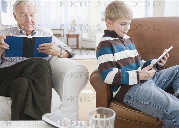 Grandfather reading book, grandson (8-9) reading e-book in living room. Photo : Jamie Grill Photography