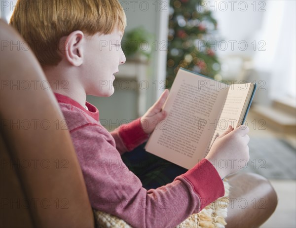Boy (8-9) reading book on Christmas Eve. Photo : Jamie Grill Photography
