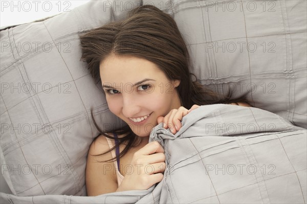 Portrait of young woman lying in bed. Photo : Mike Kemp