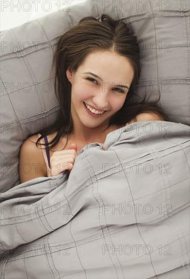 Portrait of young woman lying in bed. Photo : Mike Kemp