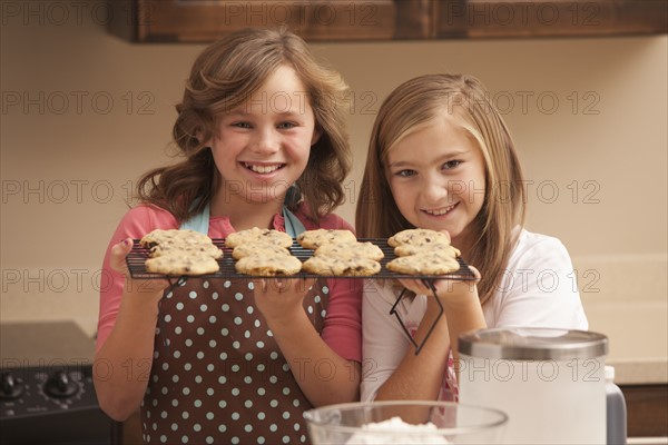 Portrait of two girls (10-11) holding biscuits in kitchen. Photo : Mike Kemp