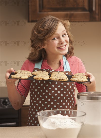 Portrait of girl (10-11) holding biscuits in kitchen. Photo : Mike Kemp