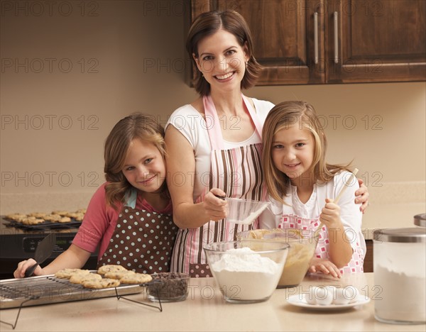 Portrait of mother baking with daughters (10-11) in kitchen. Photo : Mike Kemp