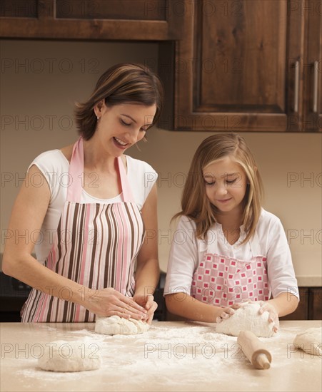 Mother and daughter (10-11) kneading dough in kitchen. Photo : Mike Kemp