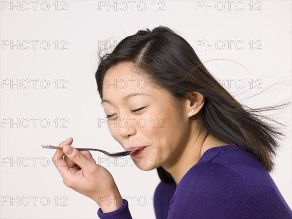 Young woman chewing spoon. Photo : Dan Bannister