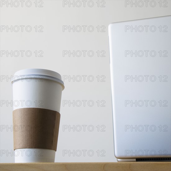 Coffee cup beside laptop in office. Photo : Joe Clark