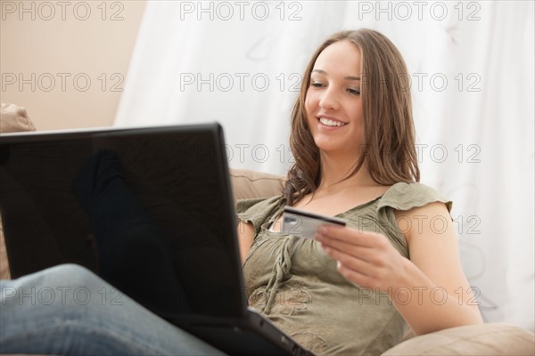 Young woman using laptop and holding credit card. Photo : Mike Kemp