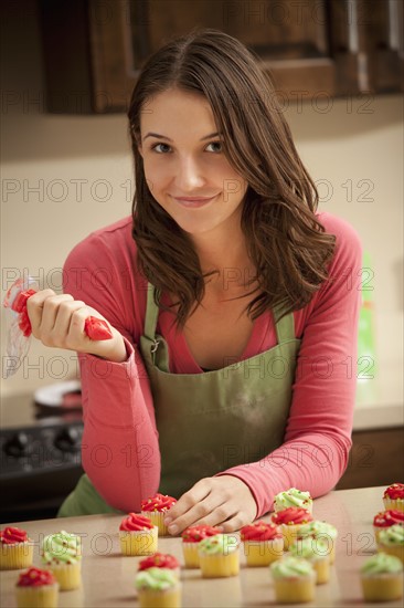 Portrait of young woman decorating cupcakes in kitchen. Photo : Mike Kemp