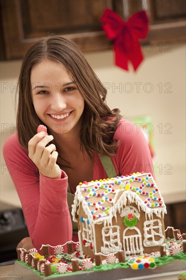 Portrait of young woman with gingerbread house in kitchen. Photo : Mike Kemp