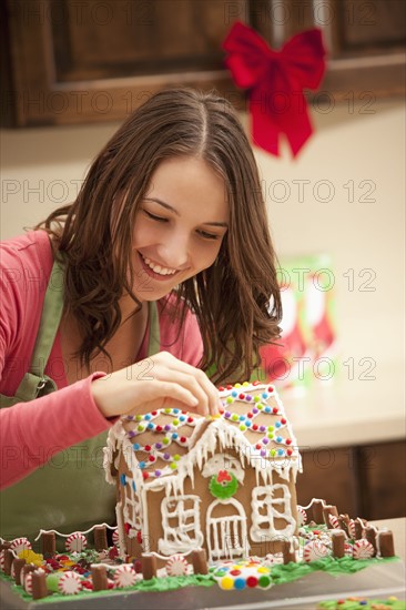 Young woman decorating gingerbread house in kitchen. Photo : Mike Kemp