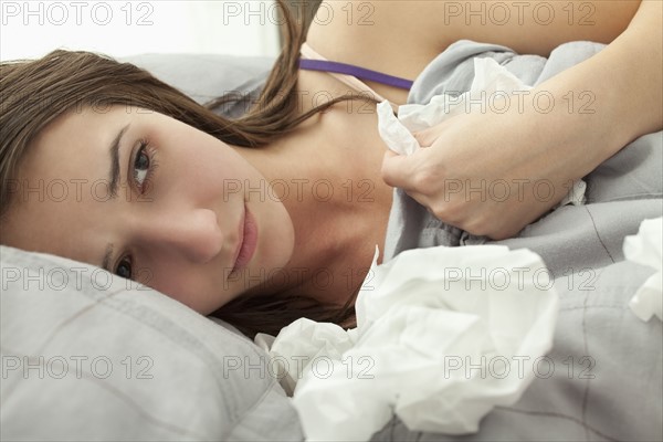 Young woman lying in bed with tissues. Photo : Mike Kemp