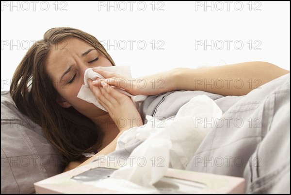 Young woman lying in bed blowing nose. Photo : Mike Kemp