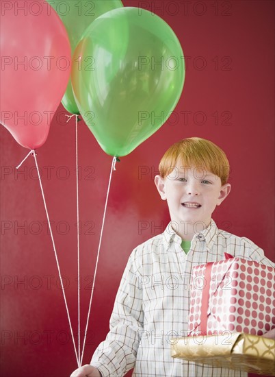 Studio portrait of boy (8-9) holding Christmas gifts and balloons. Photo : Jamie Grill Photography
