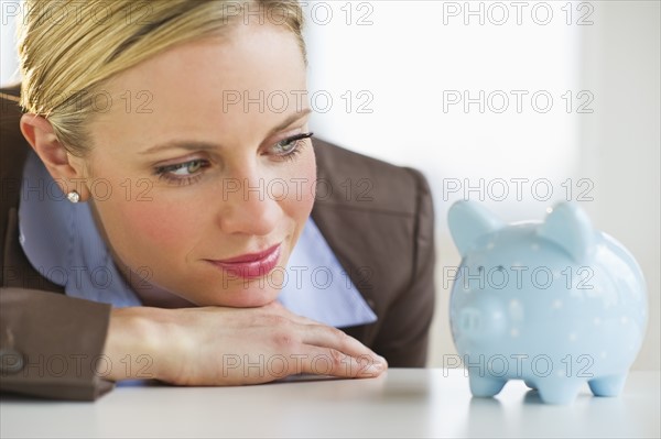 Businesswoman looking at piggy bank. Photo : Daniel Grill
