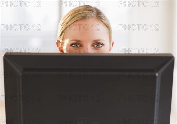 Businesswoman peeking from behind computer. Photo : Daniel Grill