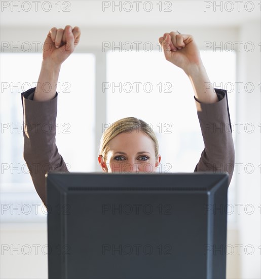 Businesswoman peeking from behind computer. Photo : Daniel Grill