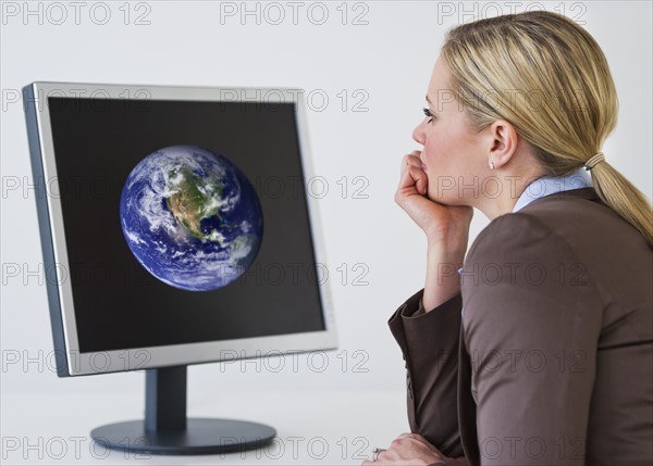 Businesswoman looking at monitor with globe. Photo : Daniel Grill