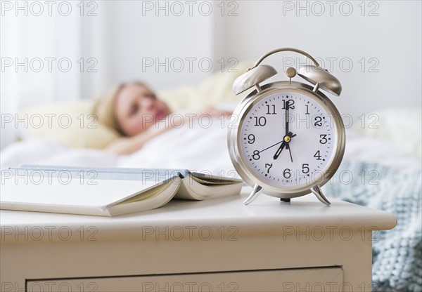 Woman in bed with alarm clock in foreground. Photo : Daniel Grill