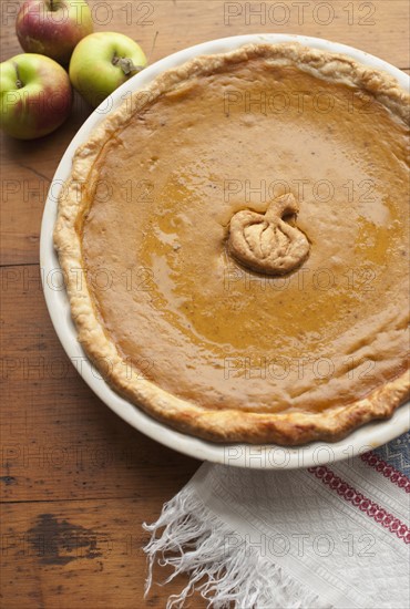 Close up of pumpkin pie and apples on table.