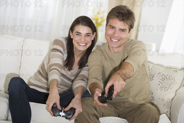 Couple sitting on sofa, playing video games.