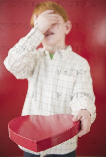 Boy (8-9) holding box of chocolates on Valentines Day. Photo : Jamie Grill Photography