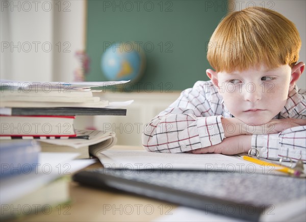 Boy (8-9) sitting at crowded desk in classroom. Photo : Jamie Grill Photography