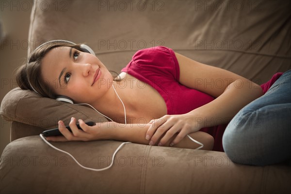 Young woman lying down on sofa and listening music . Photo : Mike Kemp