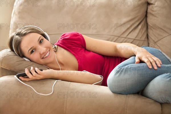 Young woman lying down on sofa and listening music . Photo : Mike Kemp