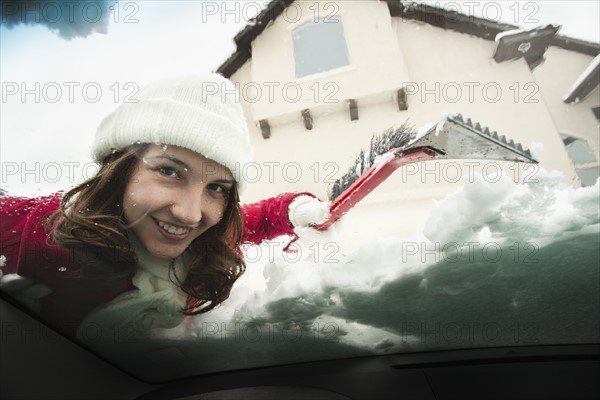 USA, Utah, Lehi, Portrait of young woman scraping snow from car windscreen. Photo : Mike Kemp