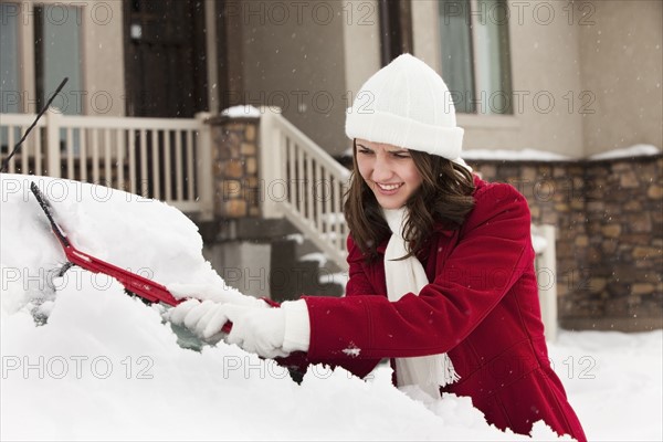 USA, Utah, Lehi, Young woman scraping snow from car. Photo : Mike Kemp