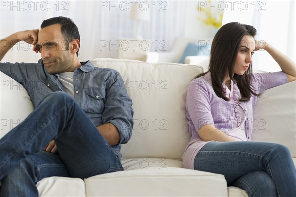 Couple sitting on sofa back to back.