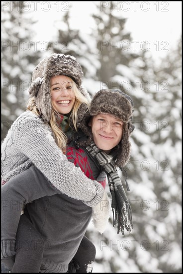 USA, Utah, Salt Lake City, man giving young woman piggy back ride in snow. Photo : Mike Kemp