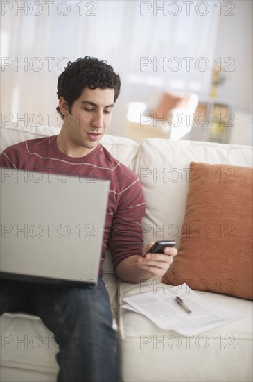 Man dialing and using laptop on sofa.