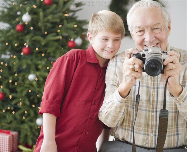 Grandfather and grandson (8-9 years) taking picture, christmas tree in background. Photo : Jamie Grill Photography