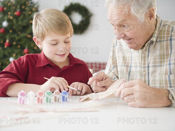 Grandfather and grandson (8-9 years) painting model airplane. Photo : Jamie Grill Photography