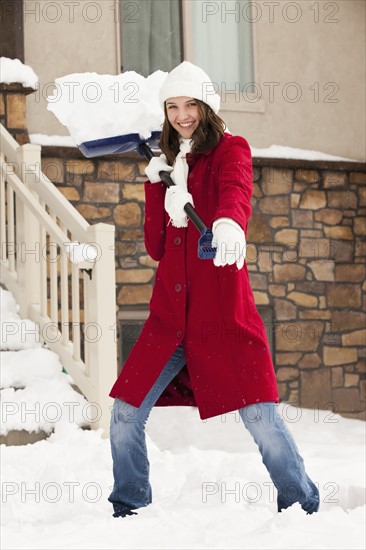 USA, Utah, Lehi, Portrait of young woman throwing snow using snow shovel. Photo : Mike Kemp