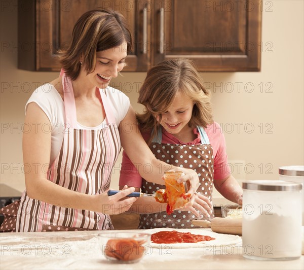 Mother and daughter (10-11) preparing pizza in kitchen. Photo : Mike Kemp