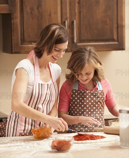 Mother and daughter (10-11) preparing pizza in kitchen. Photo : Mike Kemp