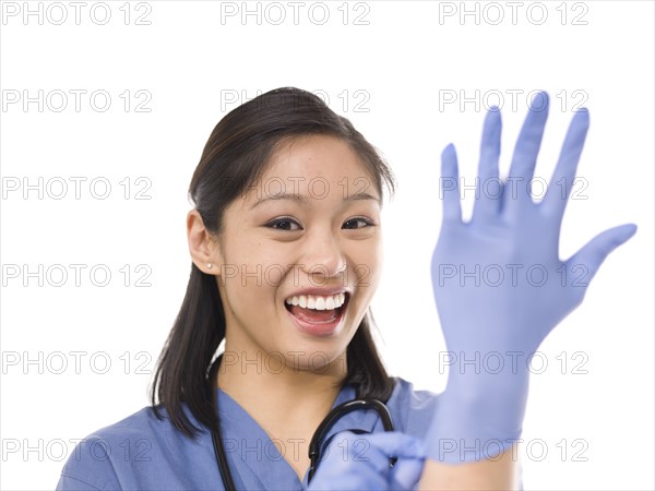 Young cheerful female surgeon putting on protective gloves. Photo : Dan Bannister