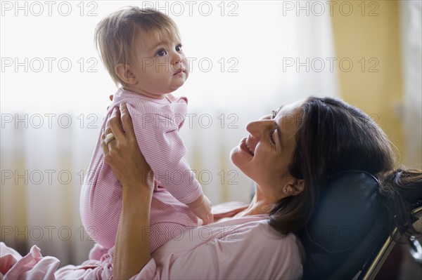 USA, California, Berkeley, Mother holding baby girl (6-11months) on sofa. Photo : Noah Clayton