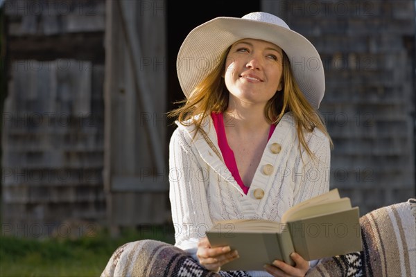 USA, California, Bolinas, Young woman reading book outdoors. Photo : Noah Clayton