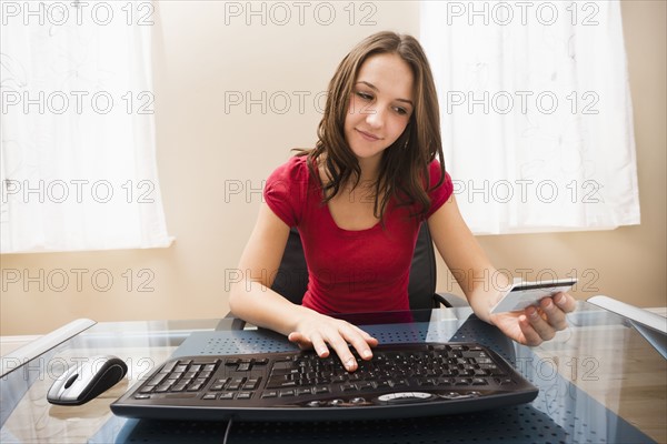 Young woman using computer and holding credit card. Photo : Mike Kemp