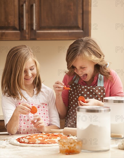 Two girls (10-11) preparing pizza in kitchen. Photo : Mike Kemp