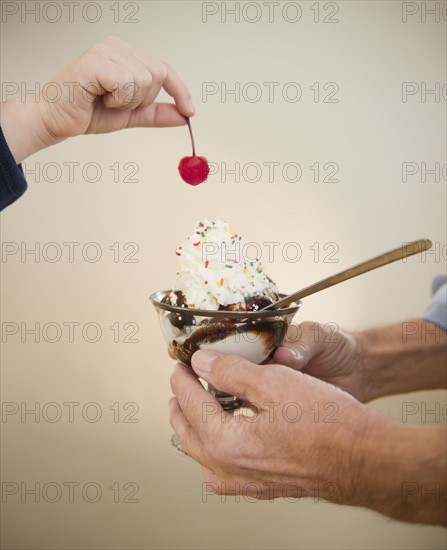 Close up of hands of grandfather and grandson (8-9) holding icecreame and cherry. Photo : Jamie Grill Photography