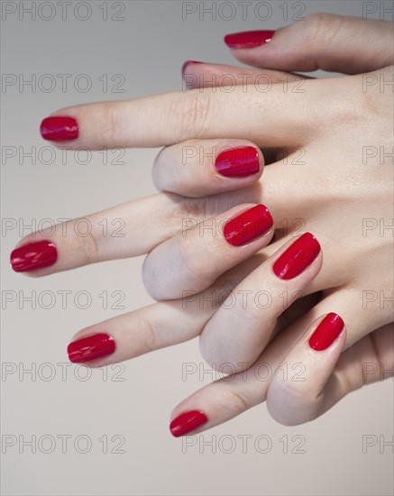 Close up of woman's clasped hands with red nail polish.