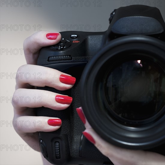 Close up of woman's hand with red nail polish holding camera.