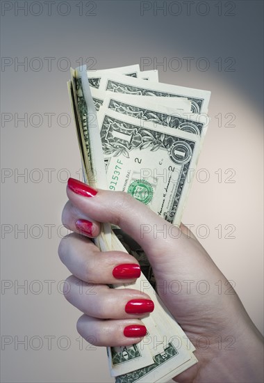 Close up of woman's hand with red nail polish holding bunch of dollar banknotes.