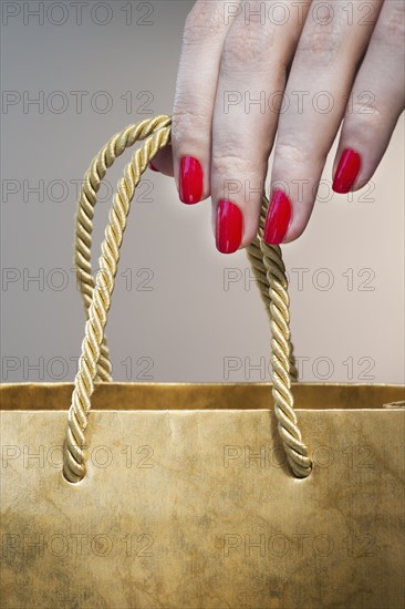Close up of woman's hand with red nail polish holding string handle of paper bag.