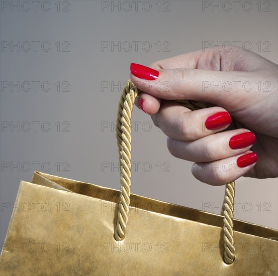 Close up of woman's hand with red nail polish holding string handle of paper bag.