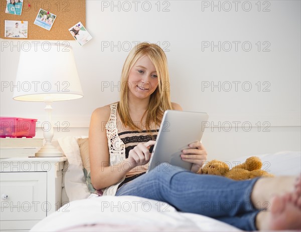 Woman sitting on bed using digital tablet. Photo: Jamie Grill Photography